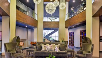 The image shows a modern living space with stylish furniture, hanging spherical light fixtures, a piano, and a staircase in the background.