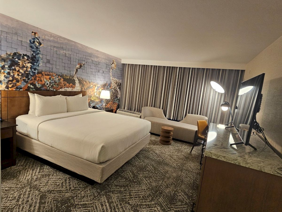 A cozy hotel room with a large bed, decorative wall art, seating area, stylish lamps, and modern furnishings.