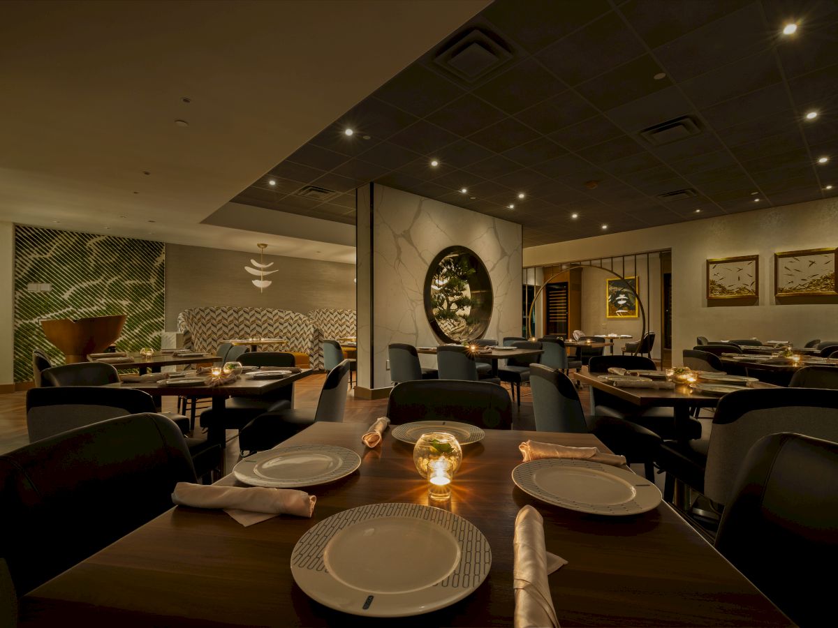 An elegant restaurant dining room with neatly set tables, cushioned chairs, warm spotlights, and modern decor in soft tones.