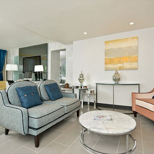 A contemporary living room with modern furniture, including a gray sofa, armchair, coffee table, and abstract wall art in a bright, cozy setting.