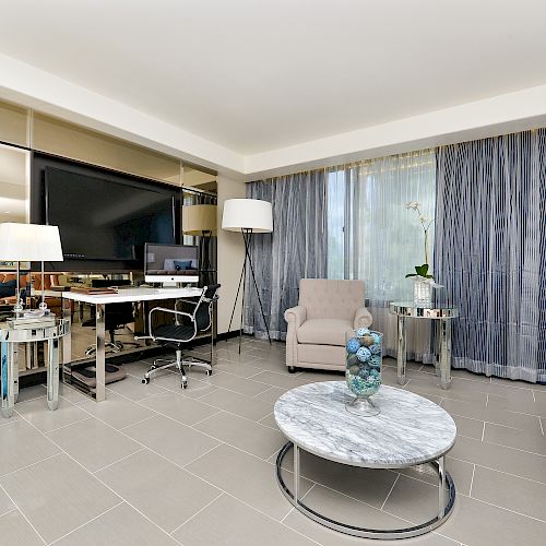 The image shows a modern living room with a TV, desk, chair, armchair, coffee table, large vases, lamps, and blue curtains, featuring clean decor.