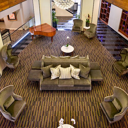 An upscale hotel lobby with a modern design, featuring comfortable seating, accent tables, a grand piano, and stylish lighting fixtures.