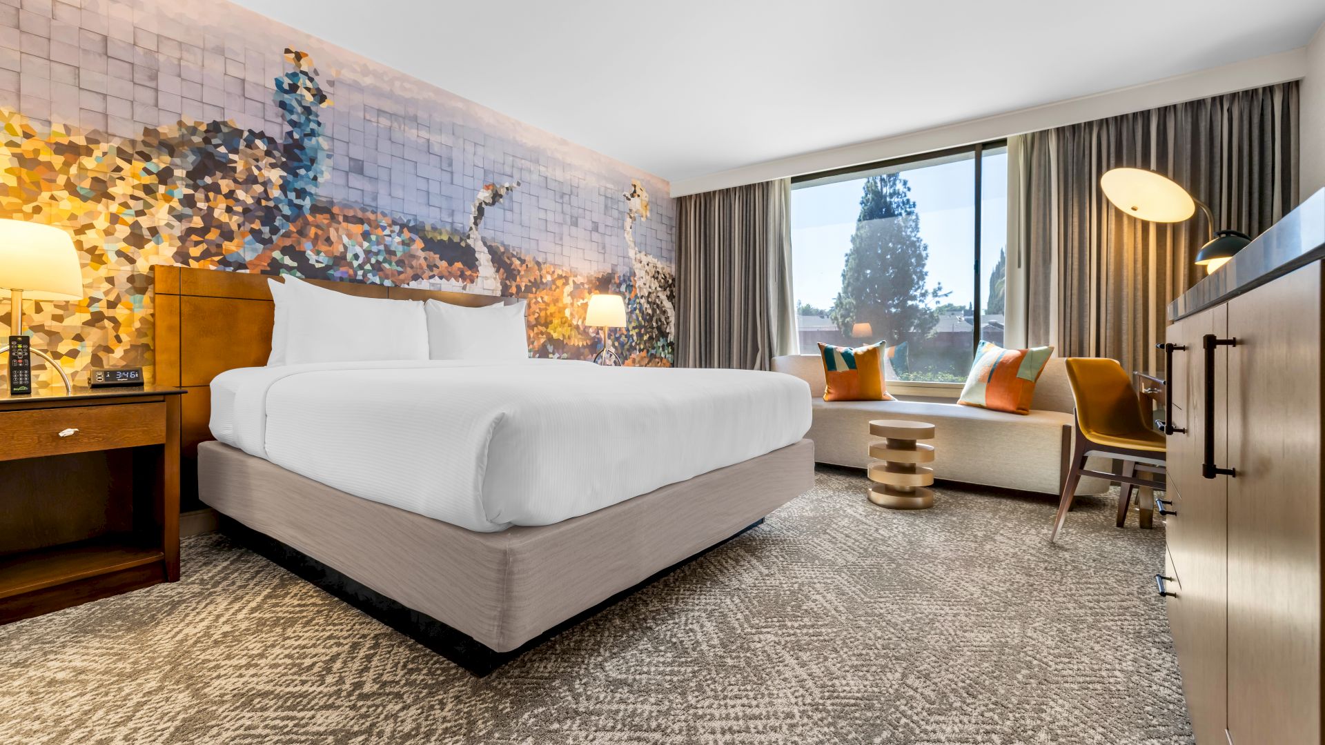 A modern hotel room with a large bed, colorful wall mural, bedside lamps, curtains, and a window.