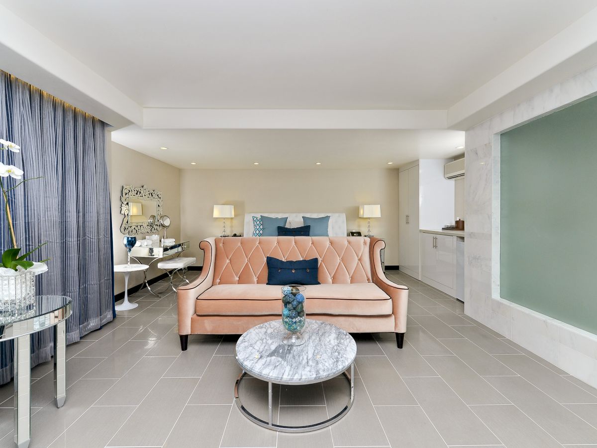 A modern, elegantly furnished living space featuring a peach sofa, marble coffee table, decorative accents, and a bed in the background, with neutral tones.