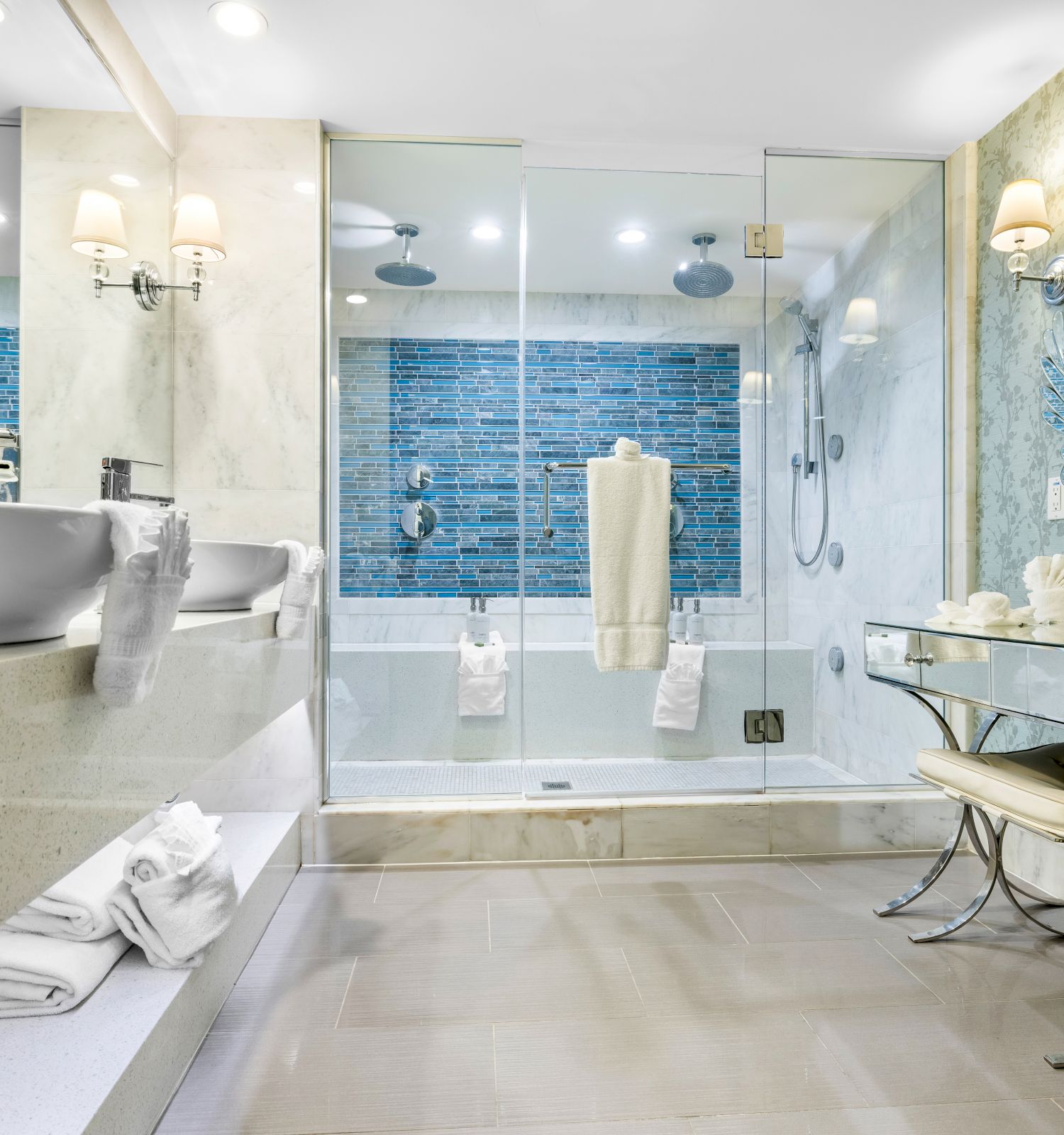 A luxurious bathroom features dual sinks, a large glass shower, elegant lighting, and decorative accents on walls and surfaces.