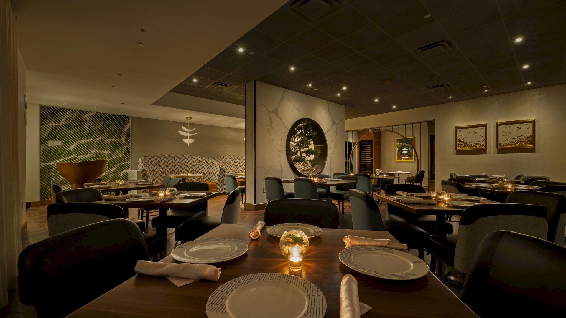A stylish restaurant dining room with set tables, warm ceiling lights, and framed wall art in a modern interior.