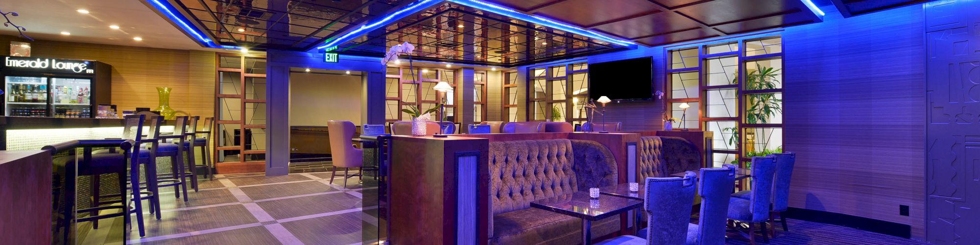 This image shows a modern lounge with blue ambient lighting, cushioned seating, tables, and a bar area in the background.