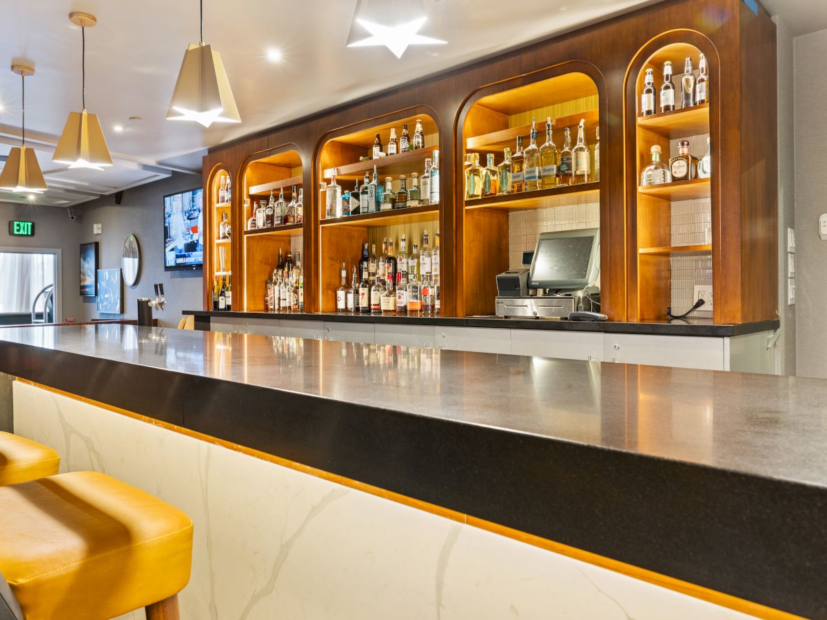 A hotel bar with a lit wooden backbar stocked with many liquor bottles, plus a sink area and indoor lighting.