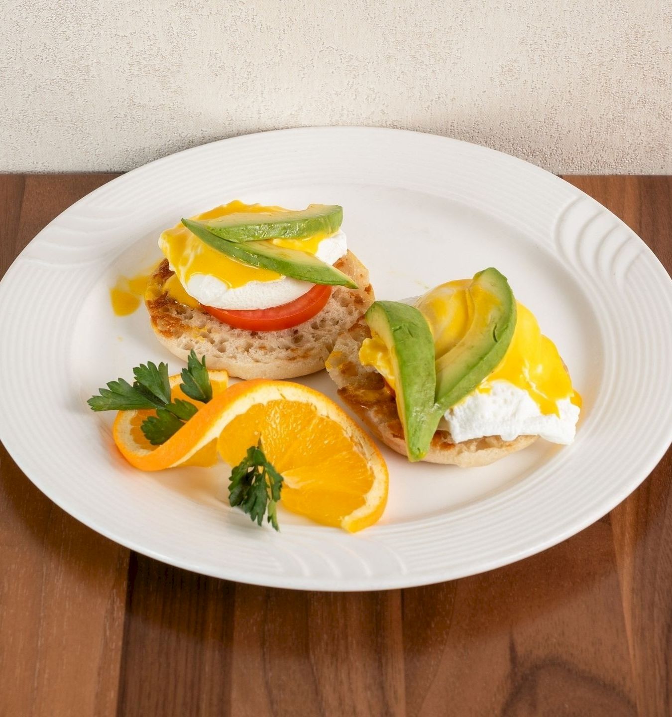 Plate of open-faced toast with sunny-side eggs, avocado, tomato, carrots, and orange slices on a white dish.