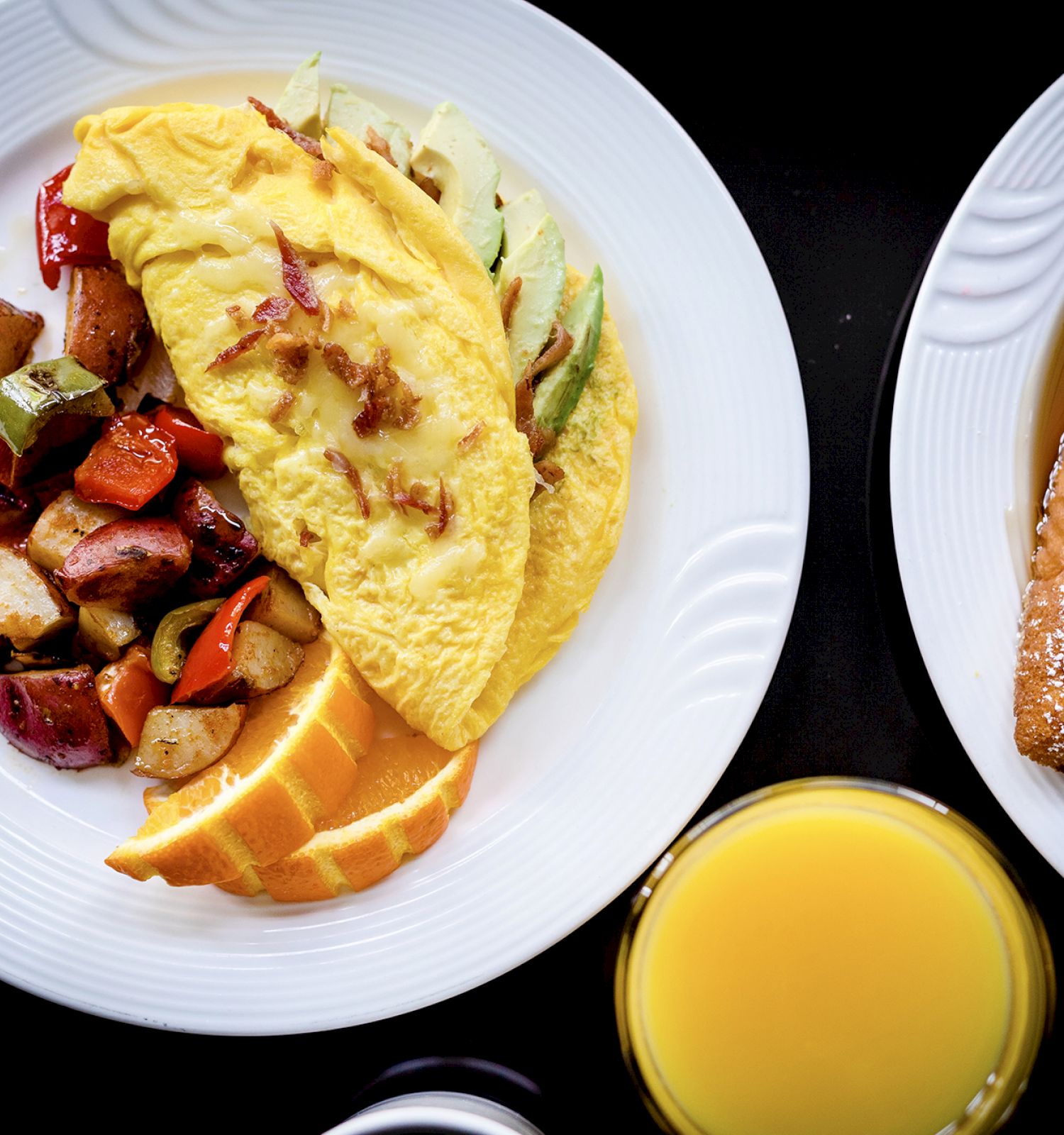 The image shows a plate with an omelet, roasted potatoes, orange slices, another plate with French toast and strawberries, and a glass of orange juice.