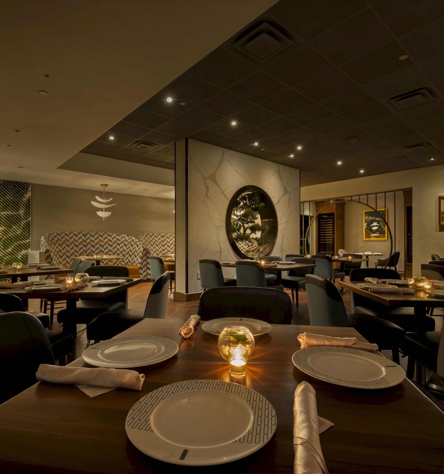 A stylish restaurant dining room with neatly set tables, soft lighting, and modern decor including framed art and mirrored walls.