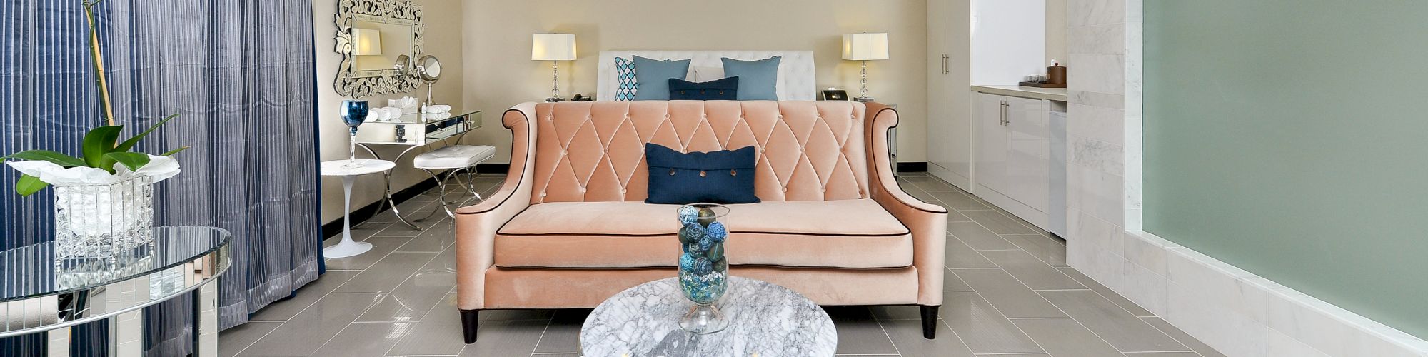 A luxurious living area with a peach sofa, marble coffee table, and modern decor includes blue accents, plants, and a well-lit ambiance, ending the sentence.