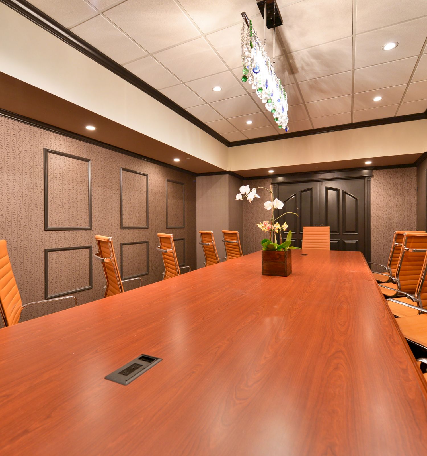 This image shows a conference room with a long wooden table, several brown leather chairs, modern decor, and ceiling lights.