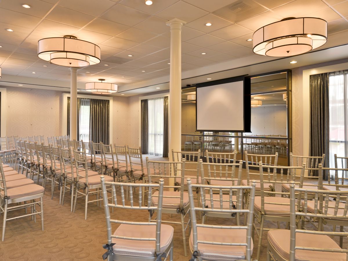 A conference room is set up with rows of chairs facing a screen, ready for a presentation or meeting.