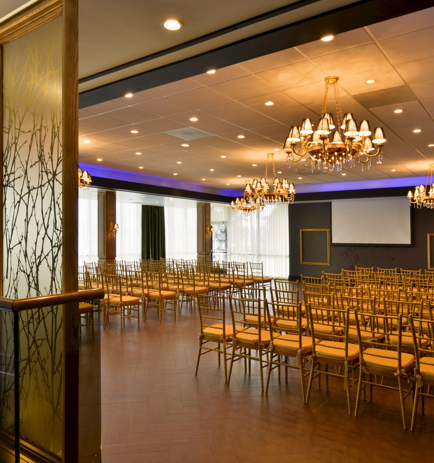 This image shows an elegant event space featuring rows of gold chairs, chandeliers, and a modern design with ambient lighting.