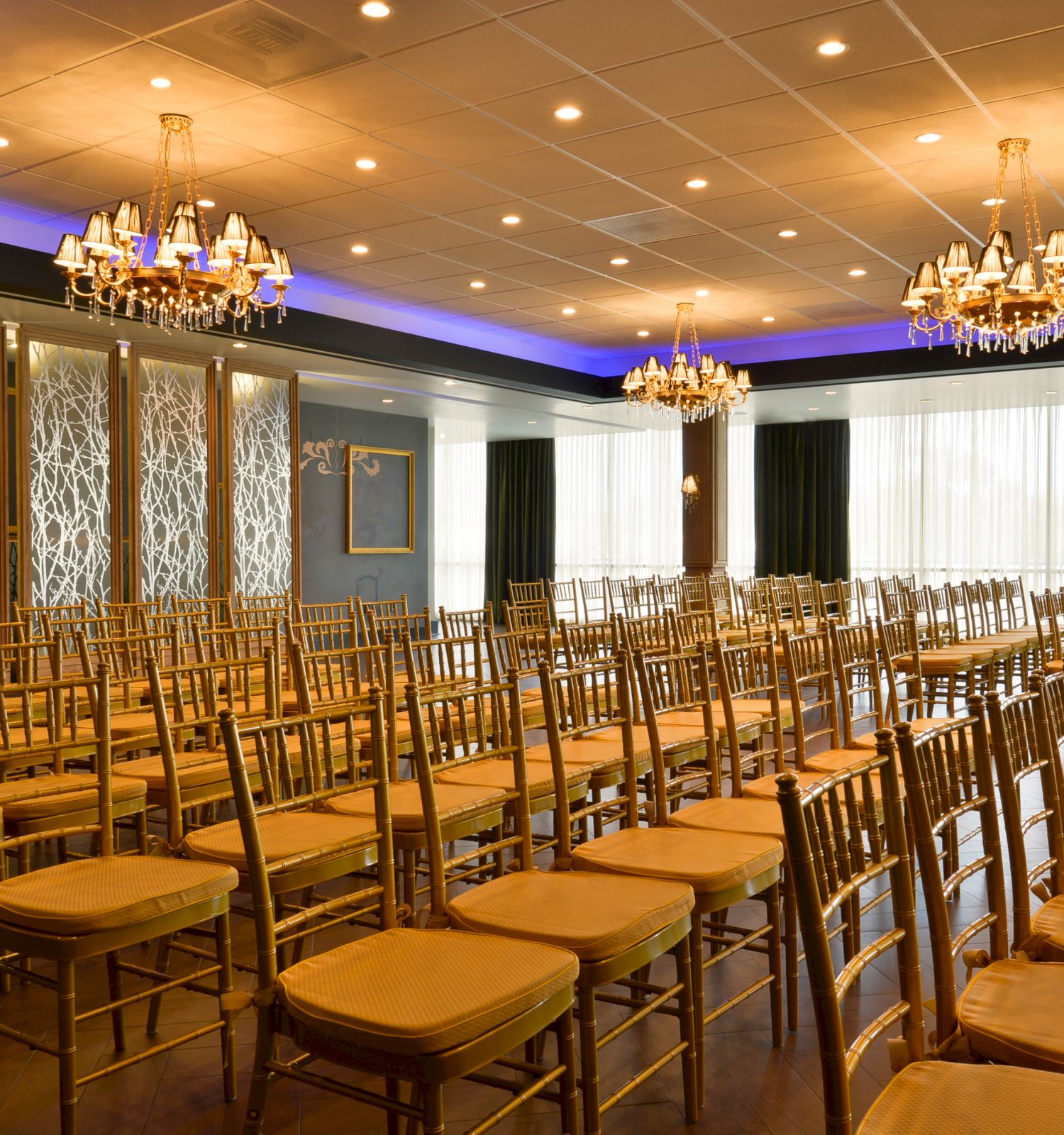 An elegant conference room set up with rows of gold chairs, chandeliers hanging from the ceiling, and decorative partitions dividing the space.