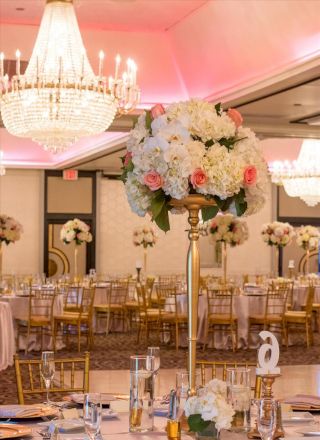 This image shows an elegantly decorated banquet hall with chandeliers, floral centerpieces, and gold chiavari chairs arranged around tables.