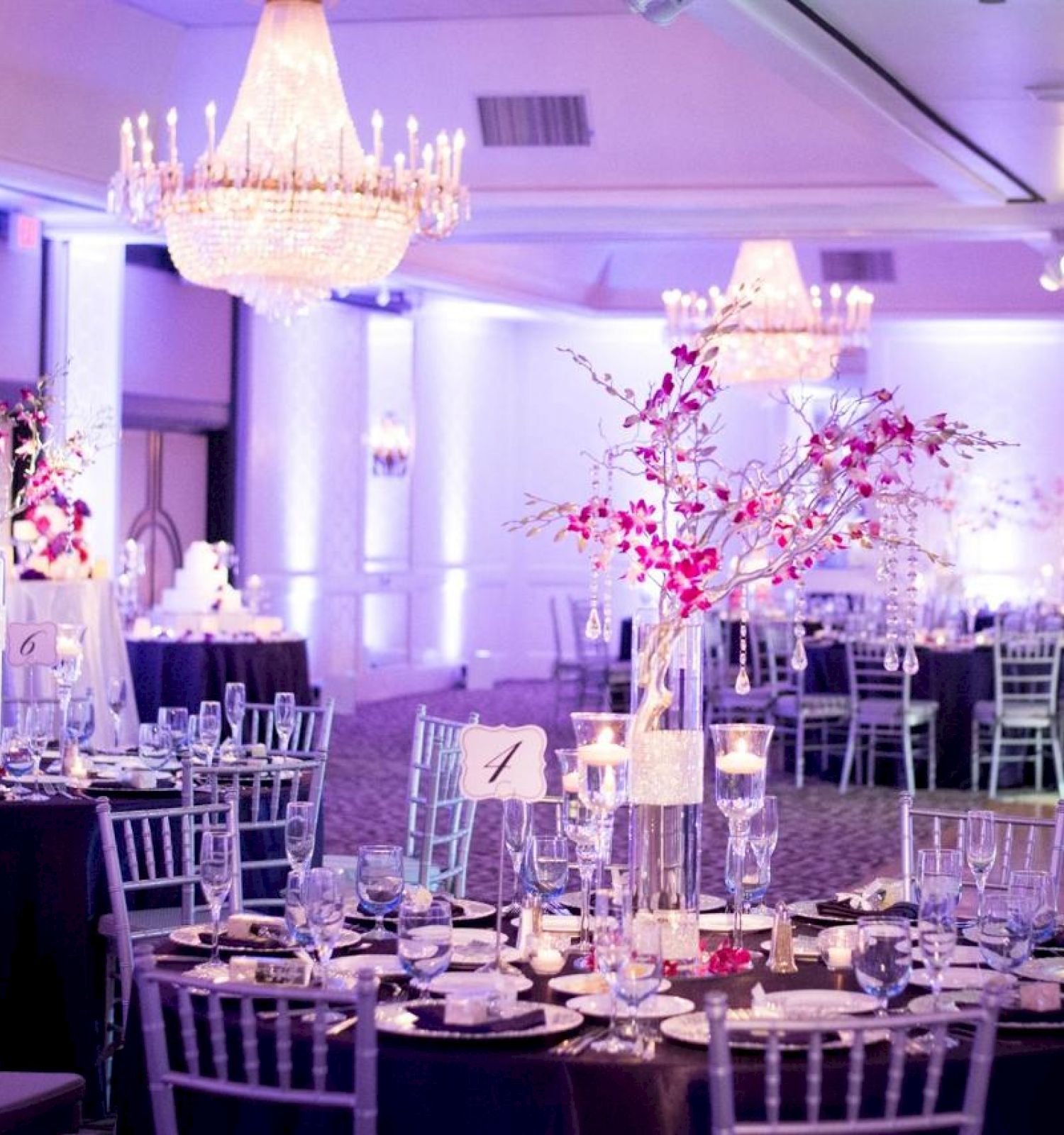 A beautifully decorated banquet hall with elegant chandeliers, floral centerpieces, round tables, and chairs set for a formal event.