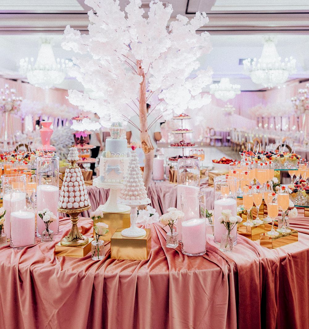 A pink-themed reception dessert table with cupcakes, drinks, and a tall white decorative tree centerpiece.