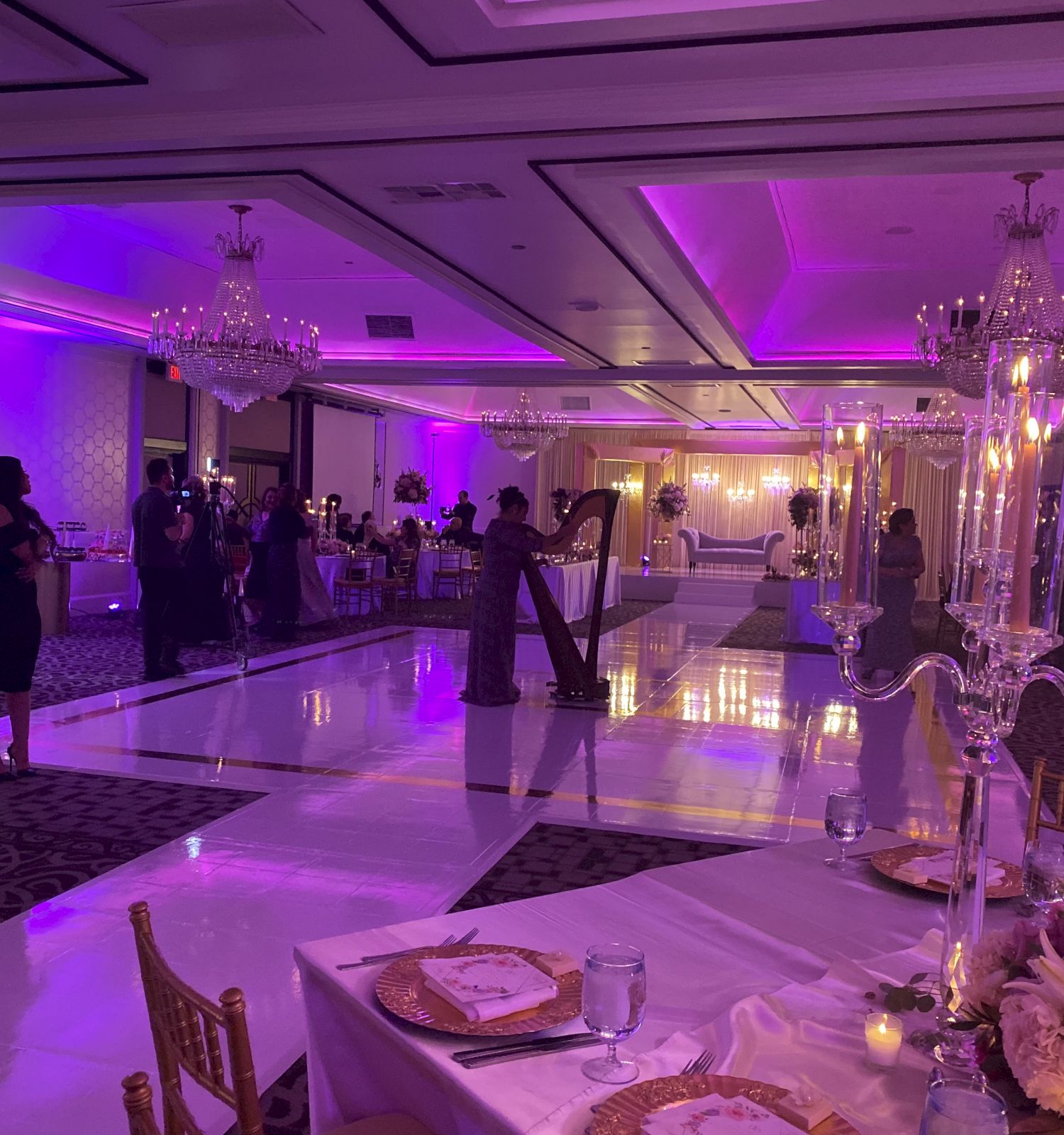 A decorated banquet hall with purple lighting, chandeliers, candles, and guests gathered around the reception tables.
