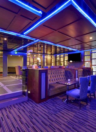 The image shows a modern lounge with blue LED lighting, cushioned seating, a bar area, and a contemporary decor.