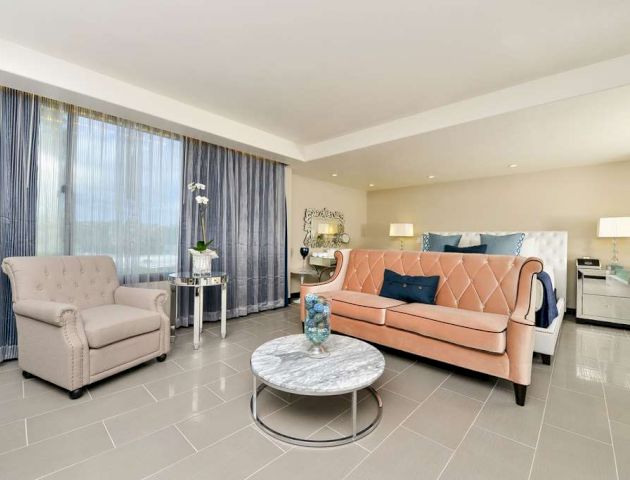 This image shows a modern, well-decorated bedroom with a sofa, armchair, coffee table, and bed, featuring neutral tones and stylish decor.