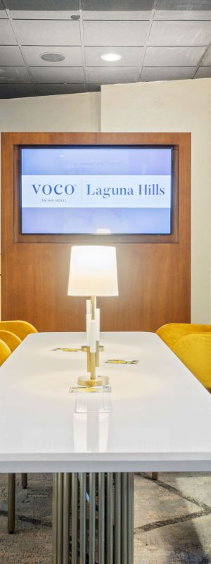 A modern hotel lounge meeting area with yellow chairs and a sign reading VOCO Laguna Hills.