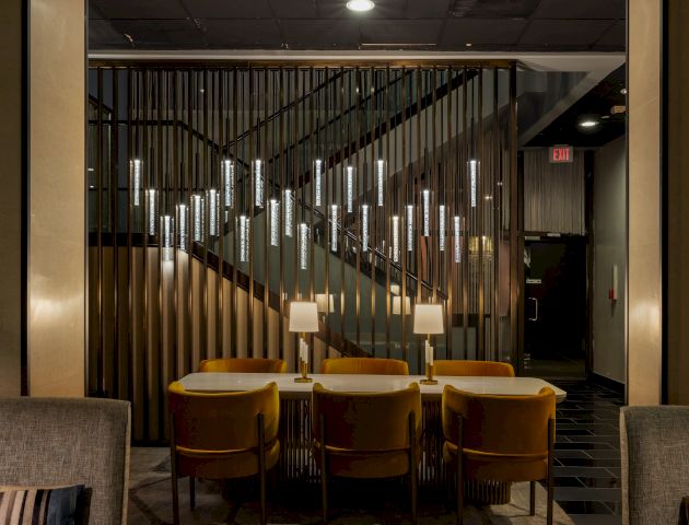 A modern hotel-like corridor with vertical glass/metal slats, warm lights, a staircase, and an &ldquo;EXIT&rdquo; sign by the hallway.