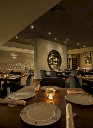A stylish restaurant dining room with set tables, warm ceiling lights, mirrored arches, and framed artwork.