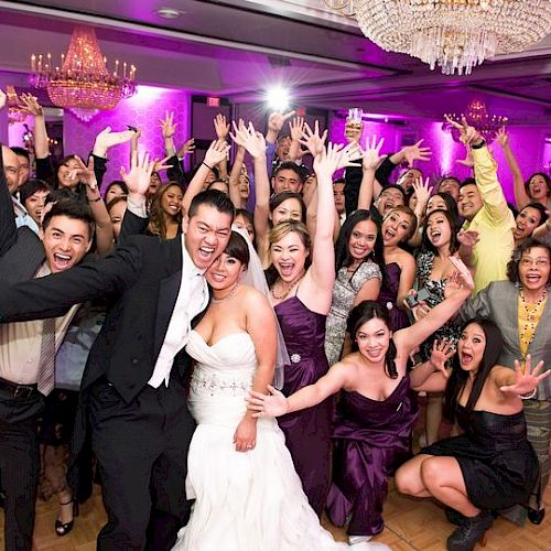 A joyful wedding celebration with the bride and groom surrounded by guests, all smiling and raising their hands in a festive, vibrant setting.