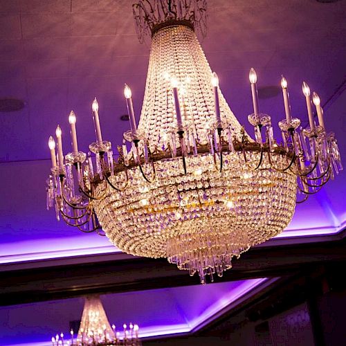 Two large, ornate chandeliers hang from the ceiling, illuminated with purple lighting in an elegant room.