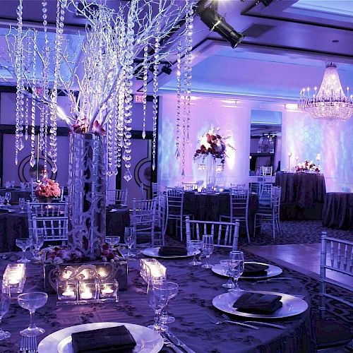 A beautifully decorated event hall features elegant table settings, chandeliers, and ambient purple lighting, creating a sophisticated atmosphere.