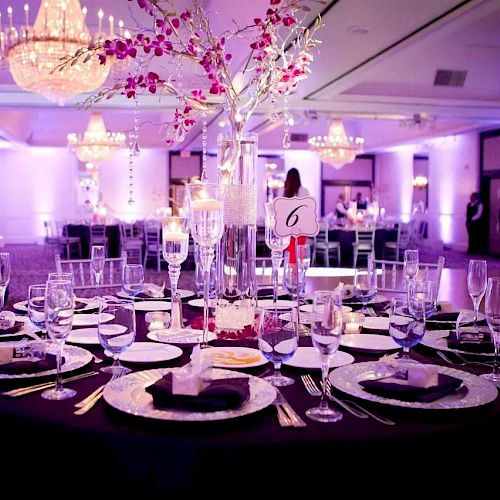 A beautifully decorated banquet table in a lavishly lit hall, set for a formal event with elegant tableware, floral centerpiece, and chandeliers.