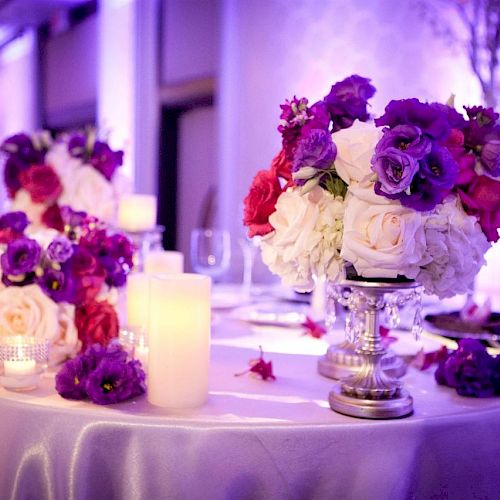 This image shows a beautifully decorated table with vibrant floral arrangements and lit candles, set in a softly-lit, elegant setting.