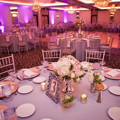 A beautifully decorated event space with round tables, flowers, candles, and elegant lighting, possibly set up for a wedding or formal celebration.