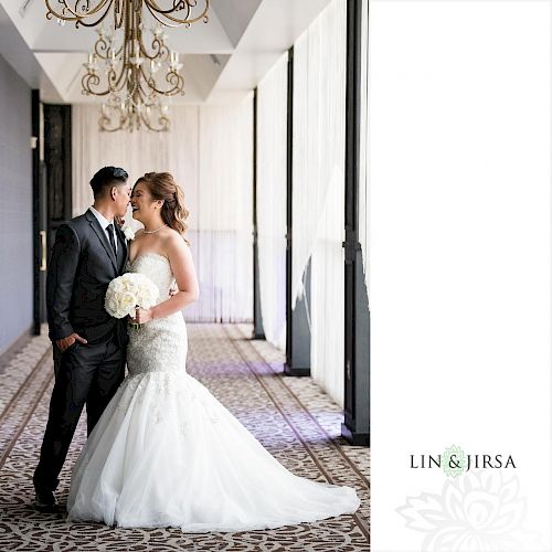 A bride in a white gown holding a bouquet stands close to a groom in a suit in a elegantly decorated hallway. LIN & JIRSA logo is visible.