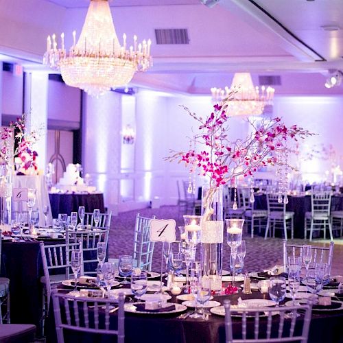 The image shows an elegant banquet hall setup with decorated tables, chandeliers, and ambient purple lighting, likely prepared for a formal event.