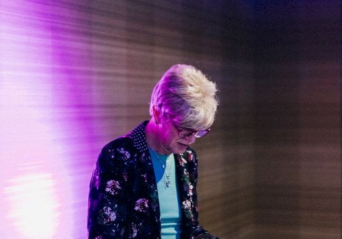 A person is playing an electronic keyboard on stage with a sign in the background that reads 