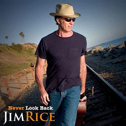 A man wearing sunglasses and a hat walks along a coastal railway track, holding a guitar. Text reads "Never Look Back" and "Jim Rice."