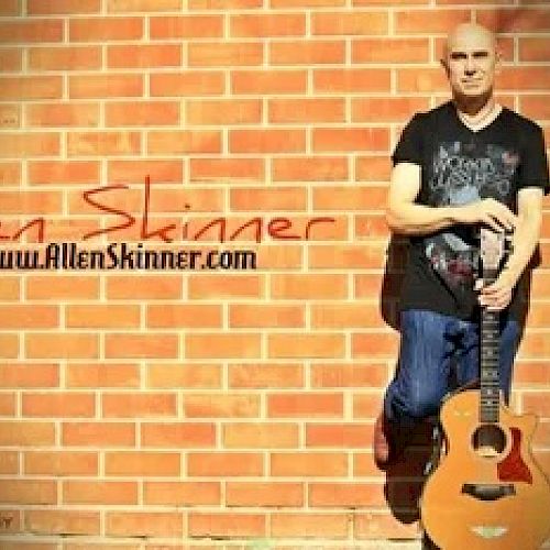 This image shows a person standing against a brick wall holding an acoustic guitar, with the text 