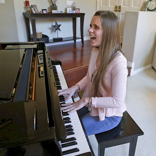 A woman is smiling and playing a piano in a well-furnished living room, sitting on a bench and having a joyful moment.