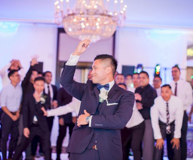 A man in a suit appears to be dancing at a formal event, with a group of people watching and cheering in the background.