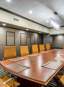 Modern conference boardroom with a long wooden table, yellow chairs, acoustic wall panels, and ceiling lights.