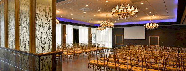 An elegant banquet hall set with gold chairs and sparkling chandeliers under warm lights.