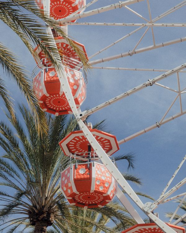 A bright red-and-white amusement ride structure with palm trees against a clear blue sky.
